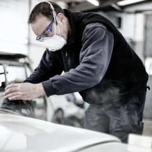 A vehicle bodywork repair technician holding sander, repairing a car